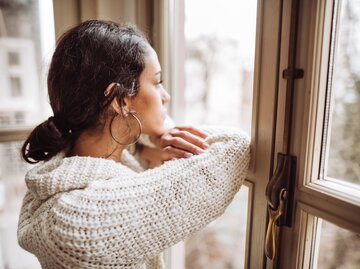 Junge Frau blickt nachdenklich aus dem Fenster | © Getty Images/franckreporter