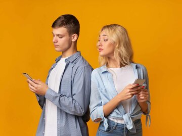 Frau schaut neugierig auf das Handy eines Mannes. | © Getty Images/Prostock-Studio