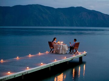 Paar sitzt beim Candle-Light-Dinner auf einem Steg am See | © Getty Images/Ronnie Kaufman
