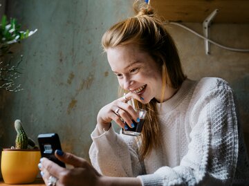 Eine junge Frau schaut verliebt auf ihr Handy | © GettyImages/Willie B. Thomas