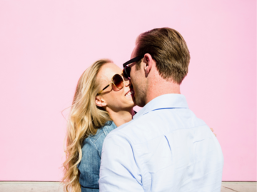 Frau und Mann küssen sich verliebt vor einer rosa Hauswand | © Getty Images/The Good Brigade
