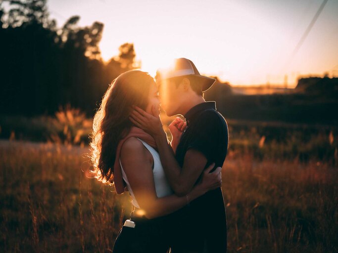 Paar steht im Sonnenuntergang und küsst sich. | © Unsplash / Chen