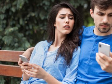 Eifersucht: Frau schaut heimlich auf das Handy ihres Freundes. | © Getty Images/Prostock-Studio