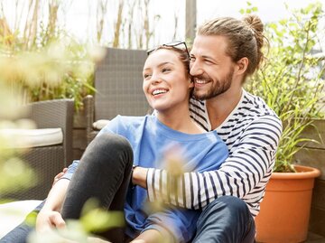 Mann und Frau sitzen umarmt auf Balkon | © Getty Images/Westend61