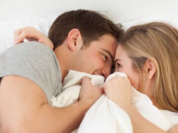 Junges Paar liegt im Bett und schaut sich leidenschaftlich in die Augen. | © Getty Images / Jamie Grill