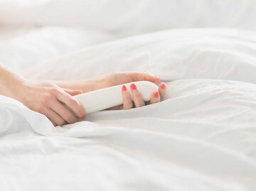 Frauenhände halten im Bett ein weißes Sexspielzeug fest. | © Getty Images / Westend61