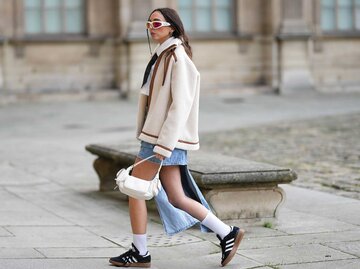 Junge Frau trägt eine beige Teddyfleece Jacke und einen A-Symetrischen Jeansrock. | © Getty Images / Edward Berthelot