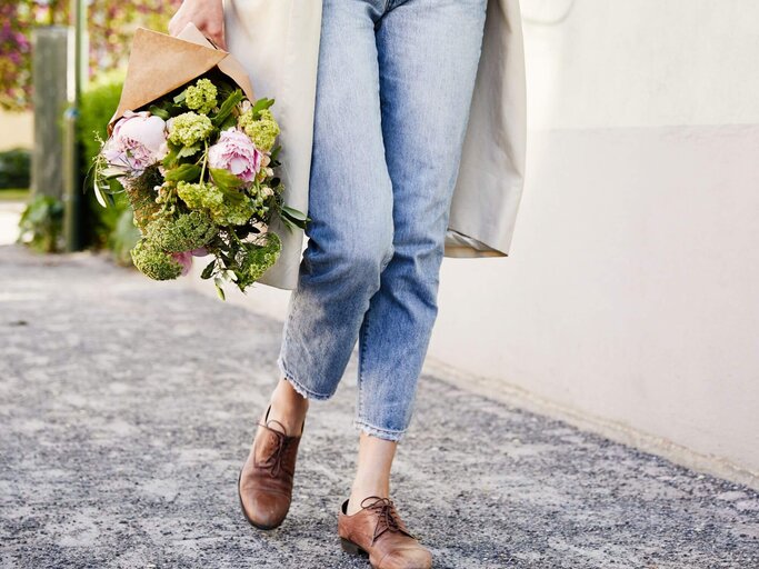 Frau mit Blumenstrauß und Boyfriend Jeans | © Getty Images/Johner Images
