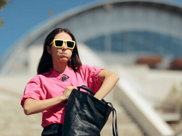 Frau mit gelber Sonnenbrille sucht genervt in ihrer großen Handtasche | © Getty Images/nicoletaionescu