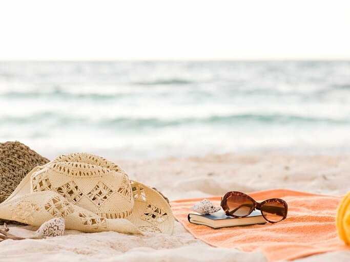 Strandtasche, Sommerhut, Strandtuch, Buch und Sonnenbrille am Strand | © Getty Images/Image Source
