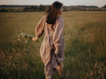Frau im Leinenkleid springt über eine Wiese | © Getty Images/Bogdan Kurylo