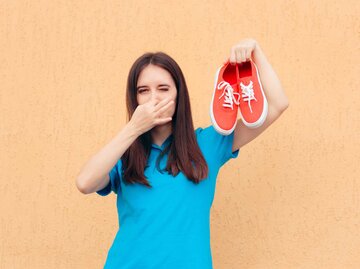 Frau hält sich die Nase zu, während sie Turnschuhe in der Hand hält | © Getty Images/nicoletaionescu