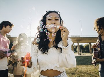 Eine junge Frau auf einem Festival bläst Seifenblasen in die Luft | © GettyImages/Maskot