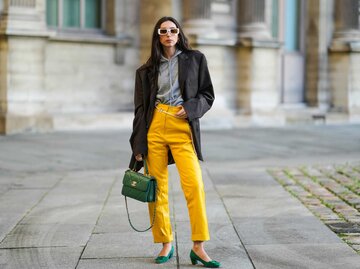 Frau trägt gelbe Lederhose, grauen Hoodie, schwarzen Blazer und grüne Henkeltasche und grüne Schuhe mit Absatz | © Getty Images/Edward Berthelot