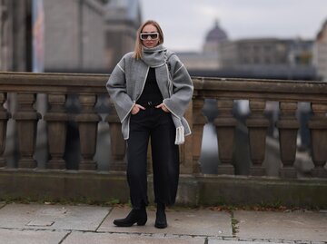 Streetstyle von Sonia Lyson in grauem Schal-Mantel, schwarzen Jeans und schwarzen Boots | © AdobeStock/Jeremy Moeller