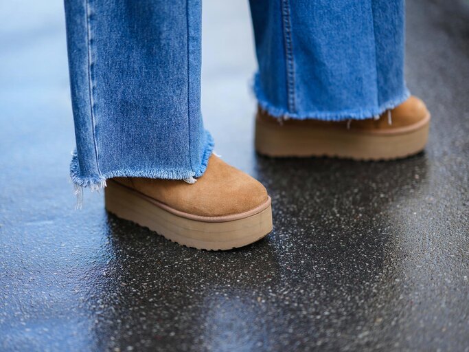 Close-up von braunen UGGs und blauen Jeans | © Getty Images/Edward Berthelot