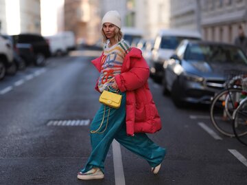 Streetstyle von Karin Teigl in blauer Cordhose, roter Daunenjacke und mehrfarbigem Strickpullover | © Getty Images/Jeremy Moeller