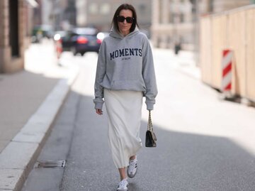 Frau trägt ein Sweatshirt, einen Satinrock, Sneakers und eine Sonnenbrille | © Getty Images/Jeremy Moeller