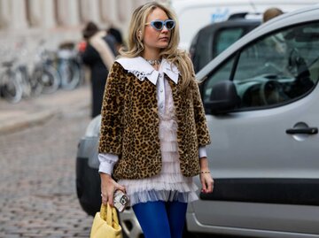 Eine Frau trägt eine Jacke mit Tierleopardenmuster, eine Rüschenbluse, eine gelbe Tasche und blaue Strumpfhosen | © Getty Images/Christian Vierig
