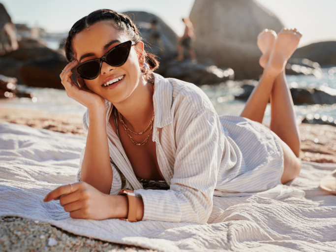 Frau liegt mit Hemdbluse und Sonnenbrille am Strand | © Getty Images/Adene Sanchez