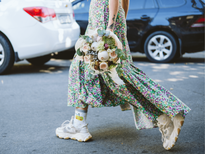 Frau in Maxikleid mit Blumenstrauß und Sneaker | © Getty Images/Iryna Khabliuk