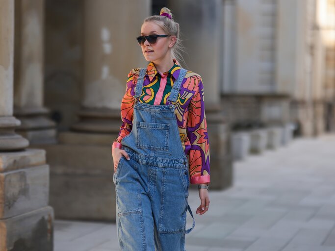 Model trägt bunt gemusterte Bluse zur Jeans-Latzhose | © Getty Images/Jeremy Moeller