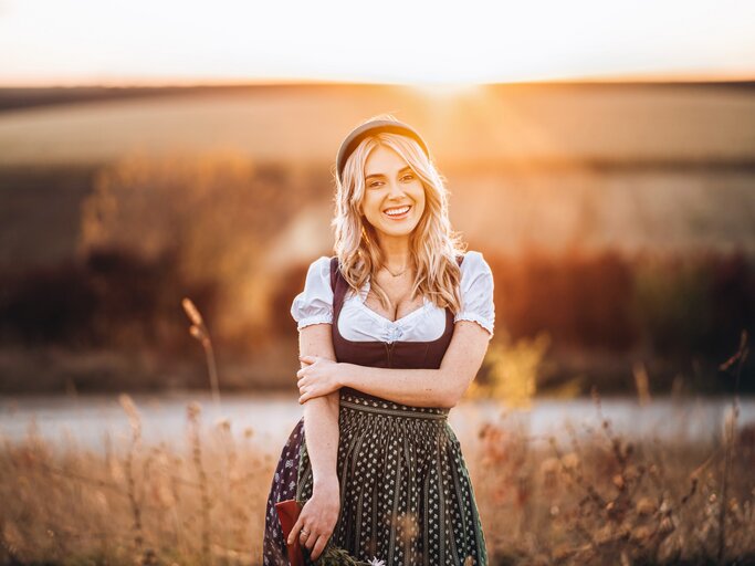 Junge Frau steht bei Sonneuntergang im Dirndl auf einem Feld | © shutterstock/bedya