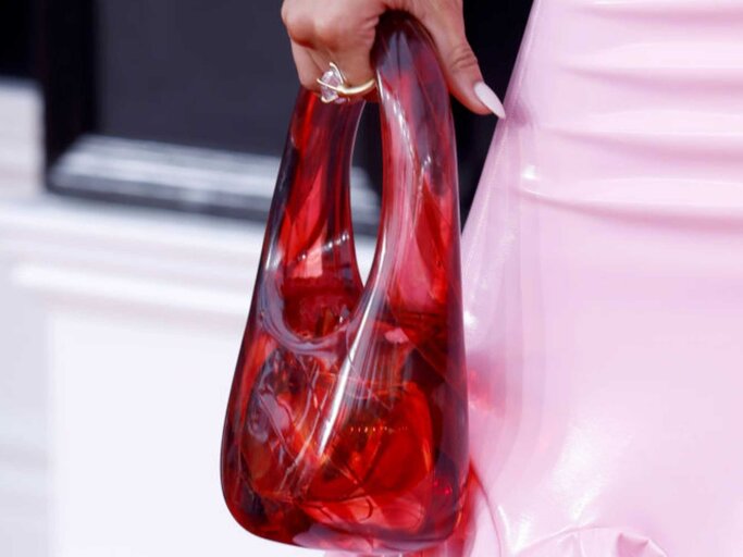 Nahaufnahme der Hand einer Frau, in der sie eine rote Handtasche aus Glas trägt | © Getty Images/Frazer Harrison