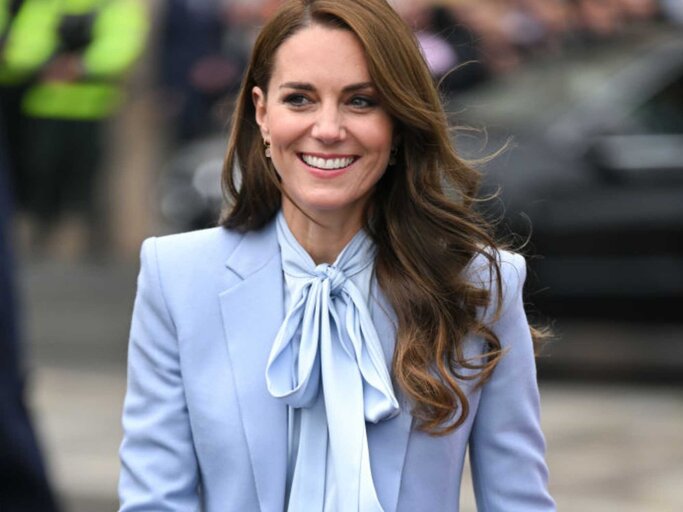 Prinzessin Kate trägt eine hellblaue Bluse, einen hellblauen Mantel und eine dunkelblaue Stoffhose und lächelt | © Getty Images/Karwai Tang 