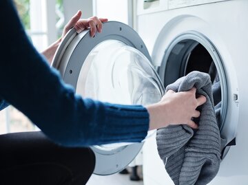 Nahaufnahme einer Frau, die Wäsche in die Waschmaschine lädt | © Getty Images/Cris Cantón