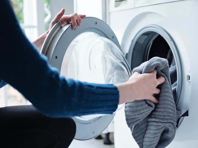 Nahaufnahme einer Frau, die Wäsche in die Waschmaschine lädt | © Getty Images/Cris Cantón