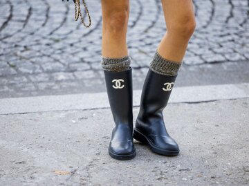 Nahaufnahme von den Beinen einer Frau, die schwarze Chanel-Stiefel und Wollsocken trägt | © Getty Images/Christian Vierig