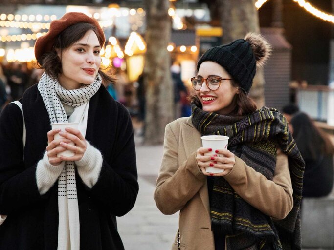 Zwei junge Frauen schlendern über einen Weihnachtsmarkt und trinken Glühwein | © Getty Images/Betsie Van der Meer