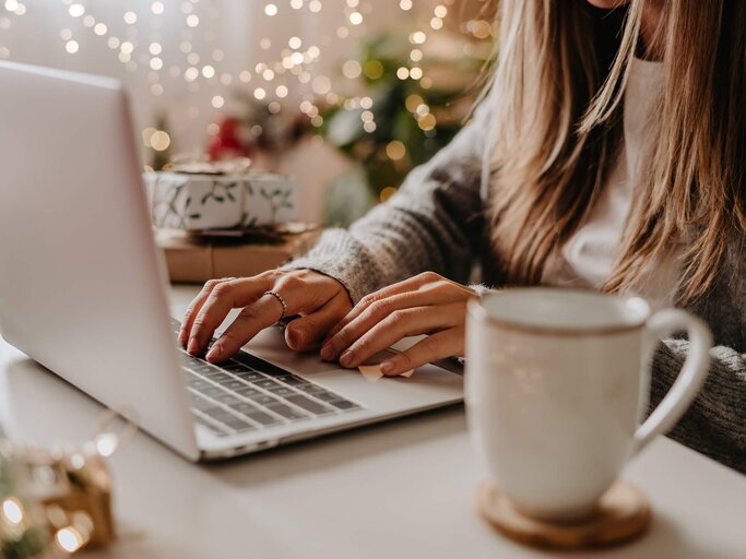 Frau sitzt mit Homeoffice Styling für den Winter aus Cardigan und Shirt am Laptop | © Getty Images/Anna Ostanina