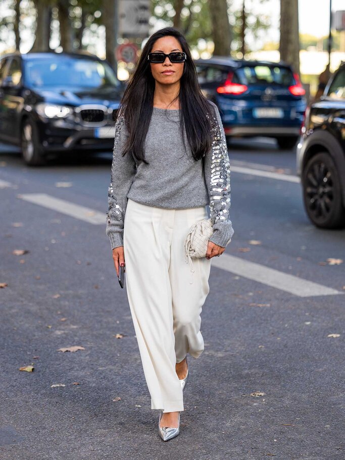 Frau trägt einen grauen Pullover mit Pailletten an den Ärmeln, dazu eine beige Culotte und silberne Pumps. | © Getty Images / Christian Vierig