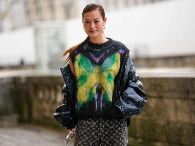 Frau trägt schwarze glänzende Daunenjacke und bunten Pullover | © Getty Images/Edward Berthelot 