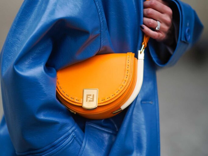 Frau trägt blauen Ledermantel und orangefarbene Halfmoon Bag | © Getty Images/Edward Berthelot 