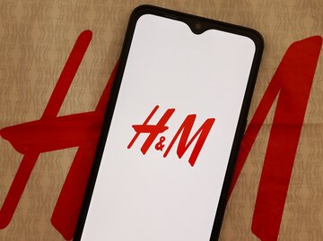 Smartphone mit geöffneter H&M-App auf brauner H&M-Tüte | © AdobeStock/Brenda Blossom