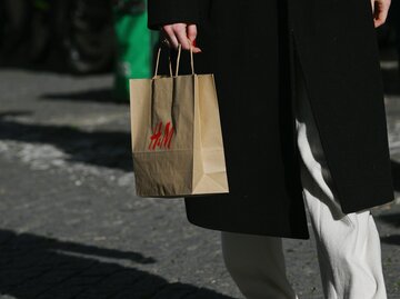 Frau in schwarzem Mantel hält braune H&M-Tüte in der Hand | © Getty Images/Zed Jameson/Bloomberg