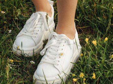 Beine einer jungen Frau in weißen Turnschuhen, die in einem Feld aus gelben Wildblumen steht | © Getty Images/Kseniya Starkova