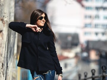 Eine Frau ist in der Stadt und trägt einen schwarzen Kurzmantel und Skinny Jeans | © GettyImages/teksomolika