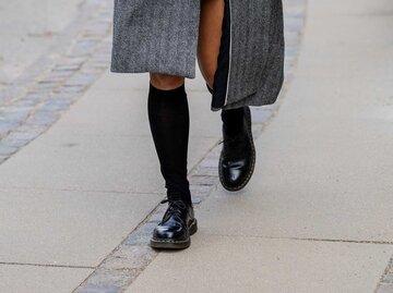 Eine Frau trägt einen grauen Mantel, schwarze Kniestrümpfe und schwarze Dr. Martens.  | © Getty Images/Christian Vierig