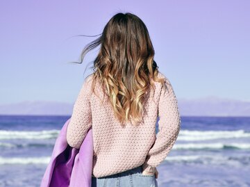 Eine junge Frau mit Beach Waves schaut auf das Meer, von hinten fotografiert. | © Unsplash.com / Pete Bellis