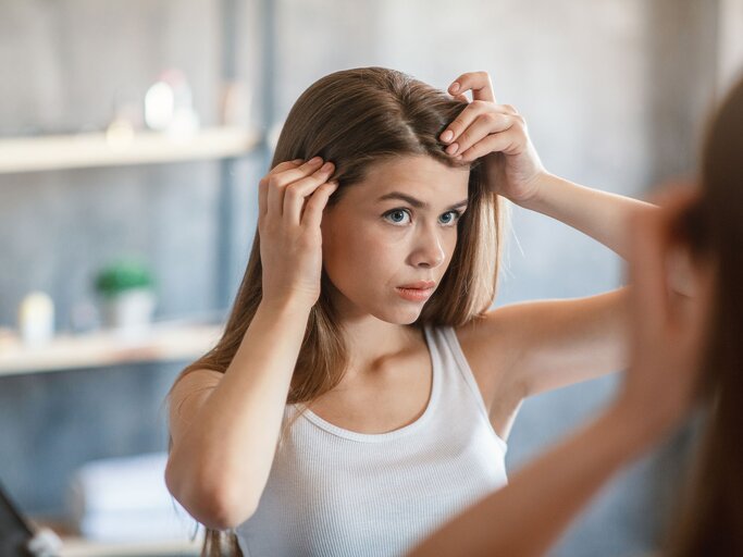 Frau betrachtet ihren Haaransatz im Spiegel | © gettyimages.de | Prostock-Studio