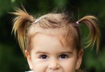 Junges Mädchen mit Pigtails sitzt auf einer Wiese uns grinst frech. | © Getty Images / Adriana Harizanova