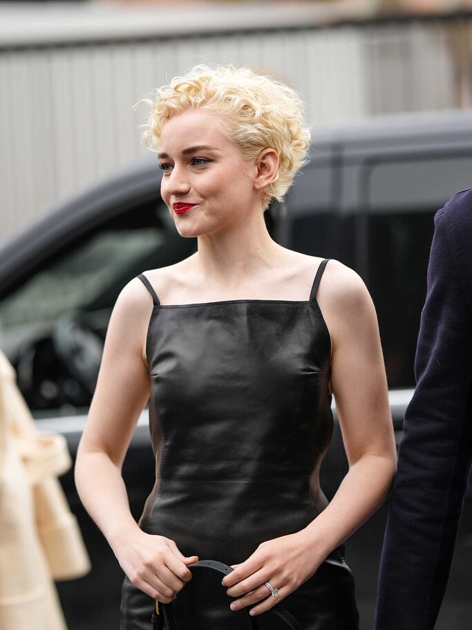 Julia Garner trägt blonde kurze Locken und ein schwarzes Lederkleid. | © Getty Images / Edward Berthelot 