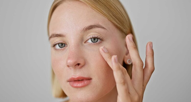 Frau tupft mit Finger über Augenringe, um die Augenringe loszuwerden. | © Adobe Stock/Krakenimages.com