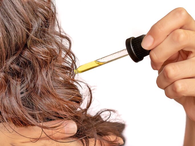Frau gibt sich mit einer Pipette Jojobaöl in die Haare | © shutterstock / Lucy Left