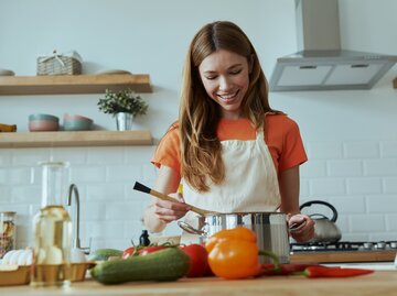 Junge Frau steht in der Küche und bereitet Essen zu  | © Getty Images/g-stockstudio