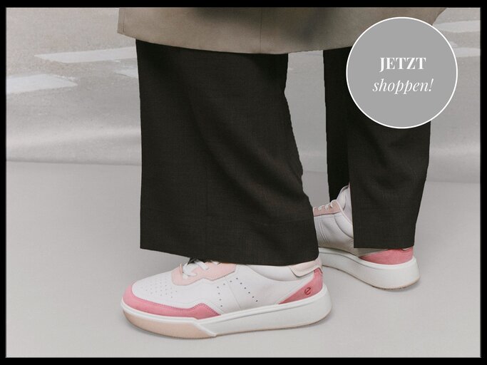 Stilvolle Kombination aus sportlichen weißen Sneakern mit rosa Akzenten und eleganten schwarzen Stoffhosen auf grauem Boden. | © ECCO/myself